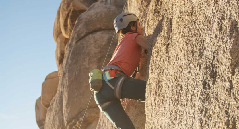 A person wearing safety gear is secured by ropes as they climb a rock wall. 